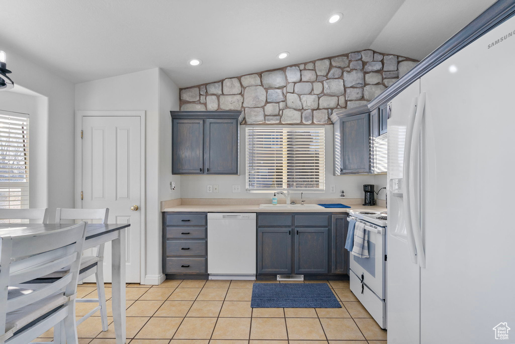 Kitchen with vaulted ceiling, white appliances, light tile patterned floors, light countertops, and a sink