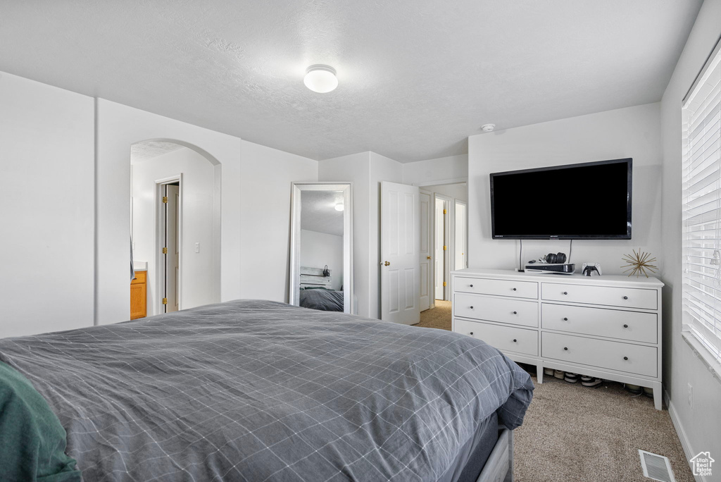 Bedroom featuring visible vents, arched walkways, and light colored carpet