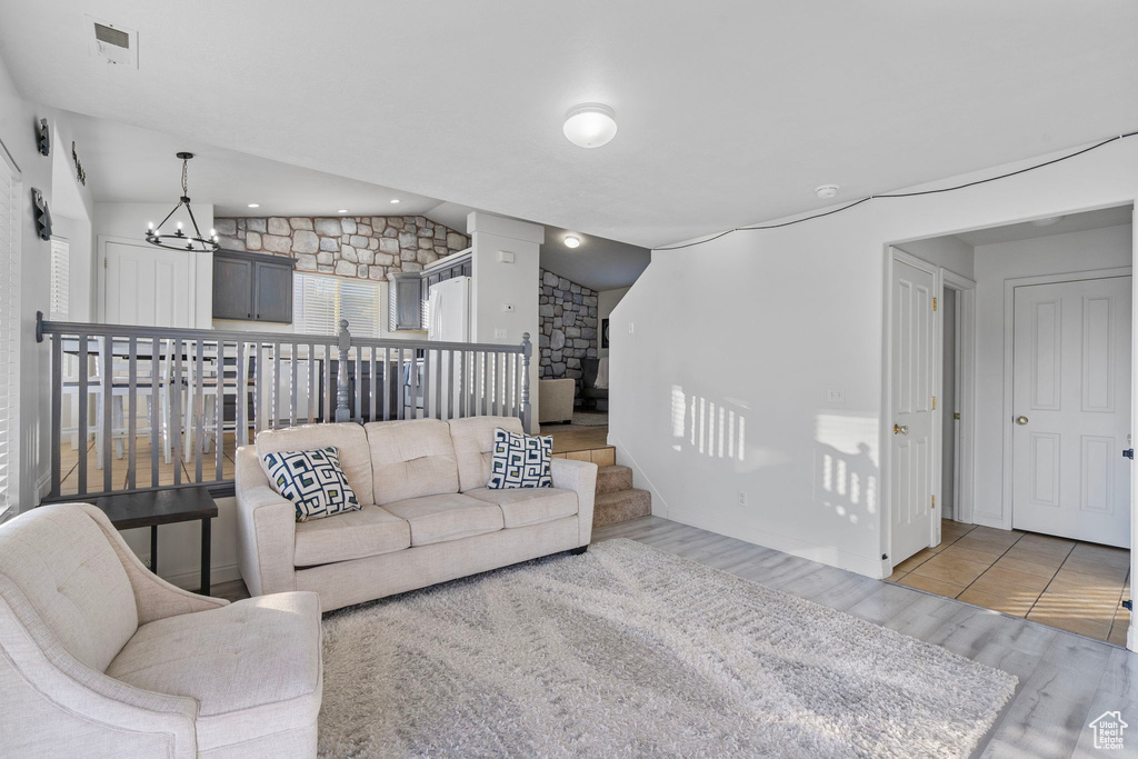 Living area with visible vents, light wood finished floors, a chandelier, and lofted ceiling