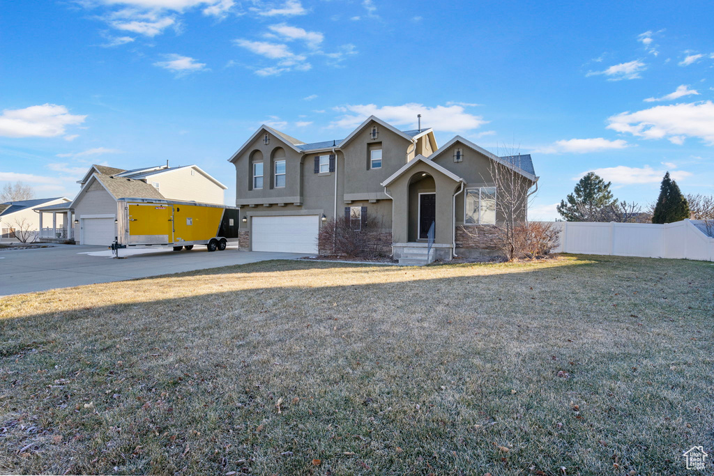 View of front facade with an attached garage, fence, concrete driveway, a front lawn, and stucco siding