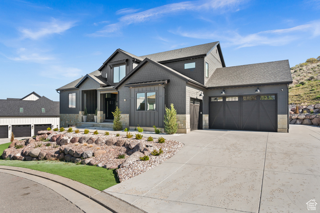 View of front of home featuring roof with shingles, stone siding, a garage, board and batten siding, and driveway