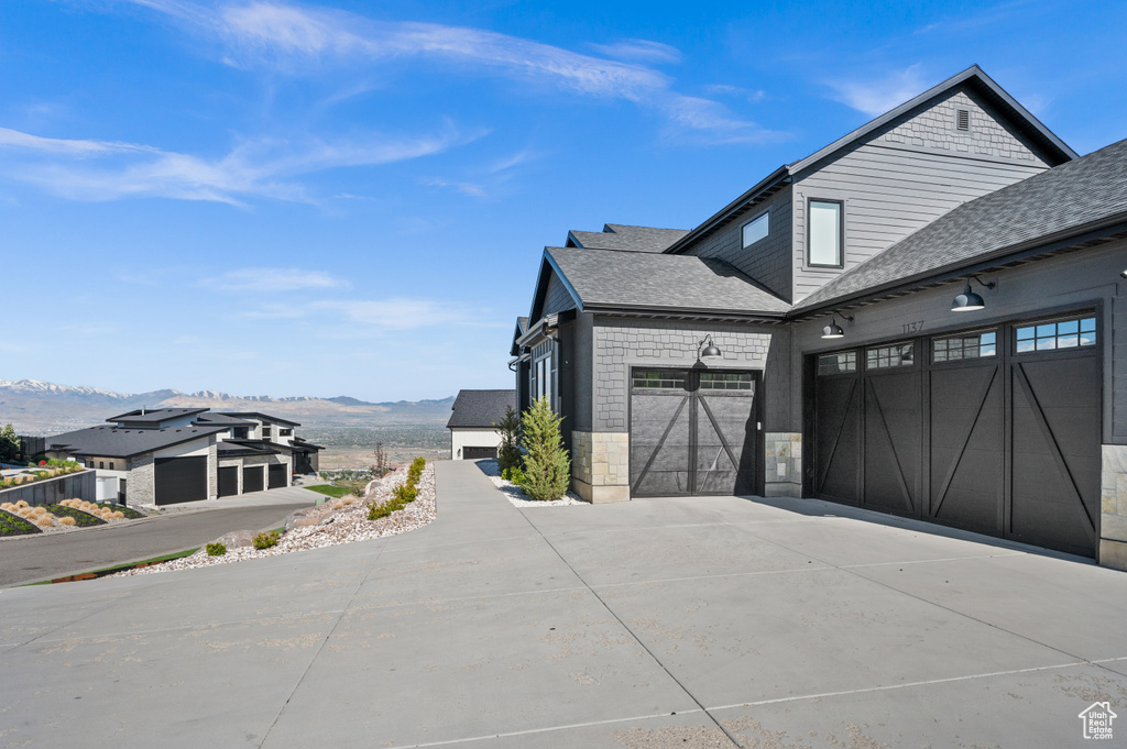 View of property exterior featuring a garage, a mountain view, a shingled roof, and driveway