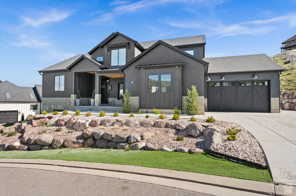 View of front of house with an attached garage, board and batten siding, stone siding, and concrete driveway