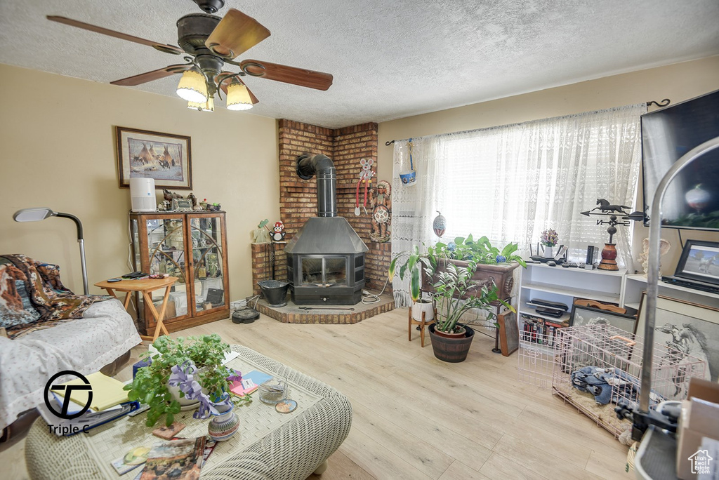 Living area featuring a textured ceiling, wood finished floors, a wood stove, and a ceiling fan