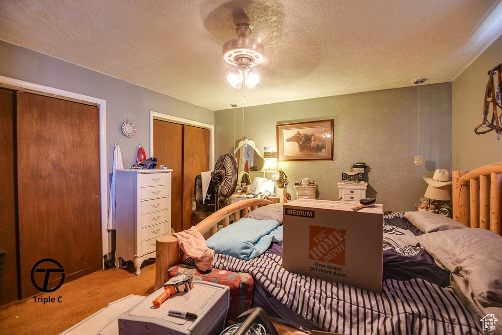 Carpeted bedroom with a ceiling fan, a textured ceiling, and two closets