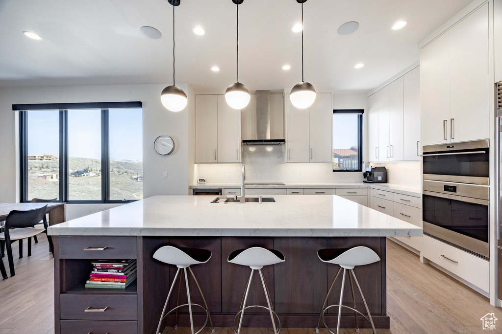 Kitchen with open shelves, a sink, wall chimney range hood, a breakfast bar, and an island with sink