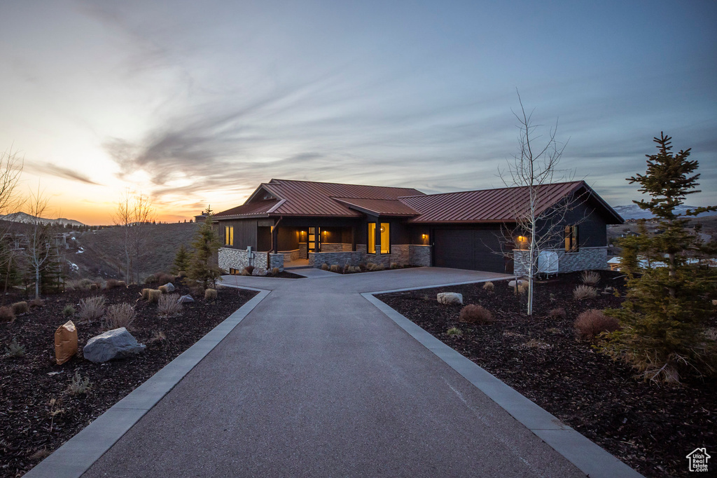 View of front of property featuring stone siding, aphalt driveway, a porch, a garage, and metal roof