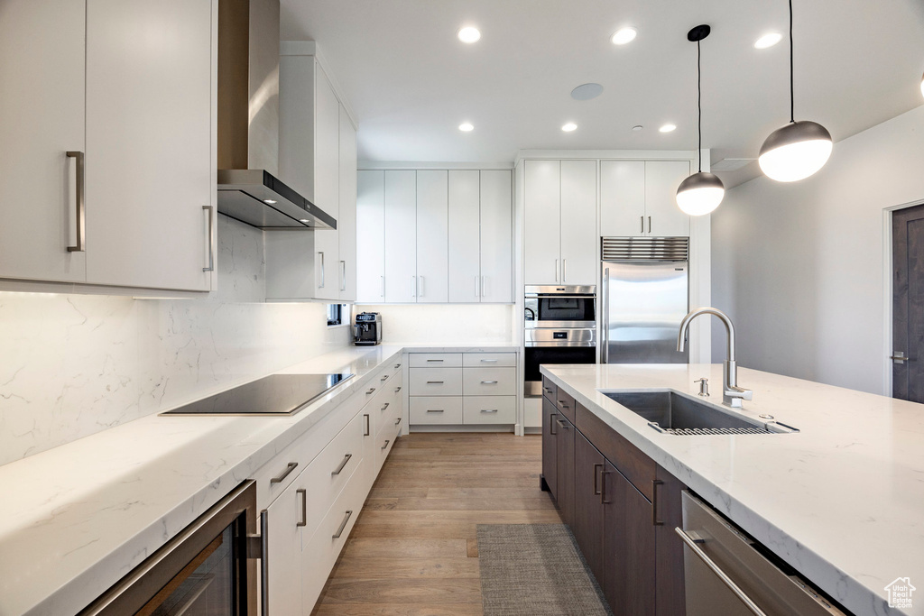 Kitchen featuring recessed lighting, wall chimney exhaust hood, appliances with stainless steel finishes, beverage cooler, and a sink