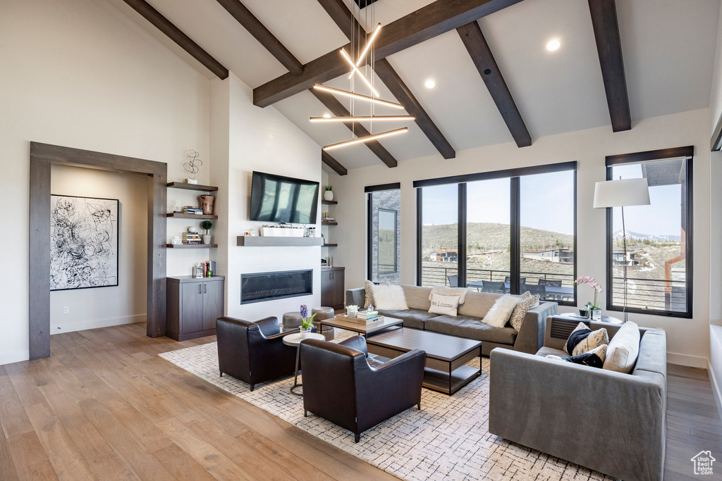 Living room featuring high vaulted ceiling, a glass covered fireplace, baseboards, and beam ceiling