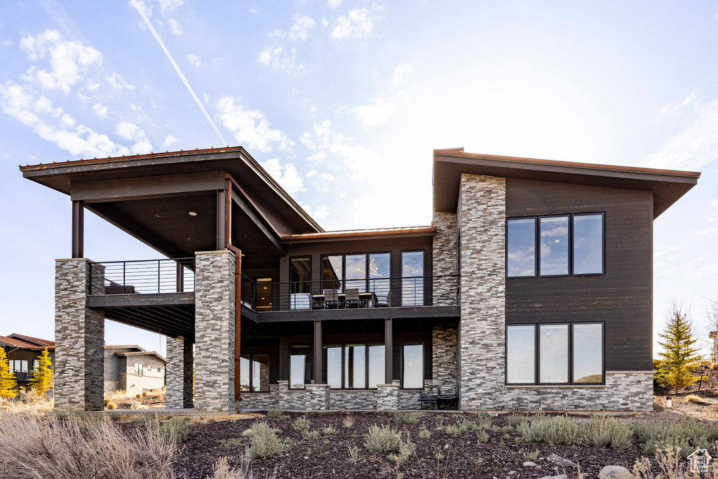 Rear view of house featuring stone siding and a balcony
