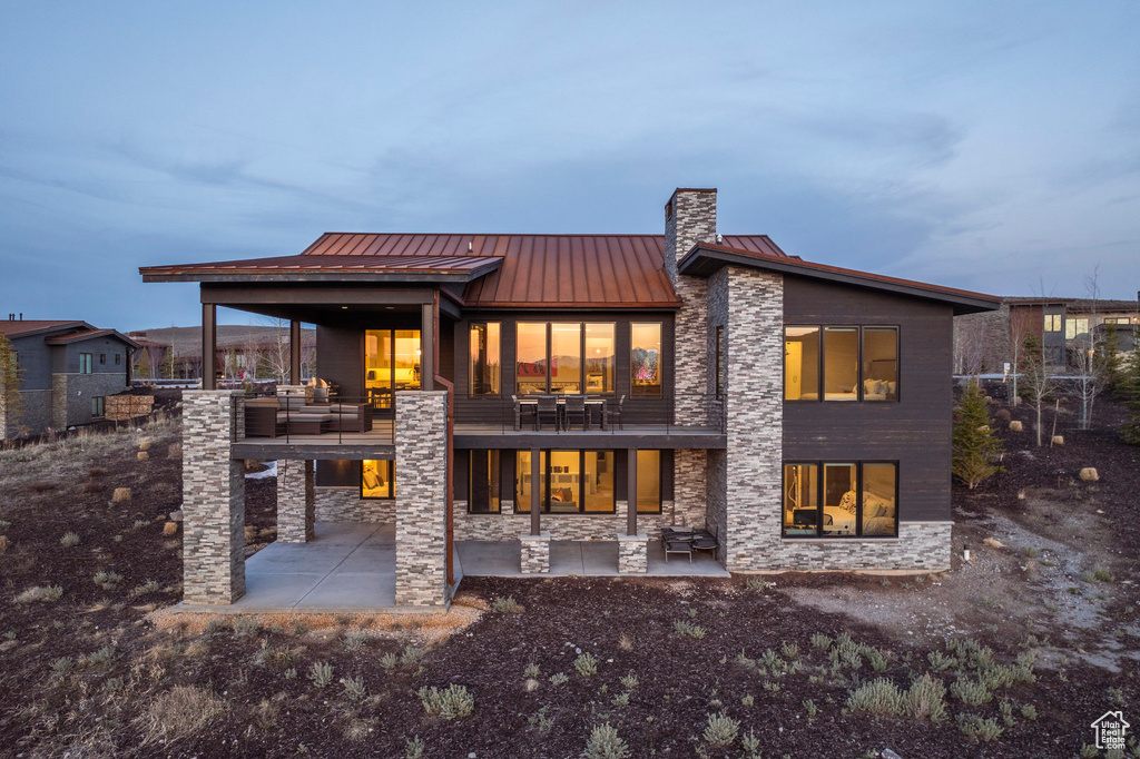 Back of property with a patio area, stone siding, metal roof, and a standing seam roof