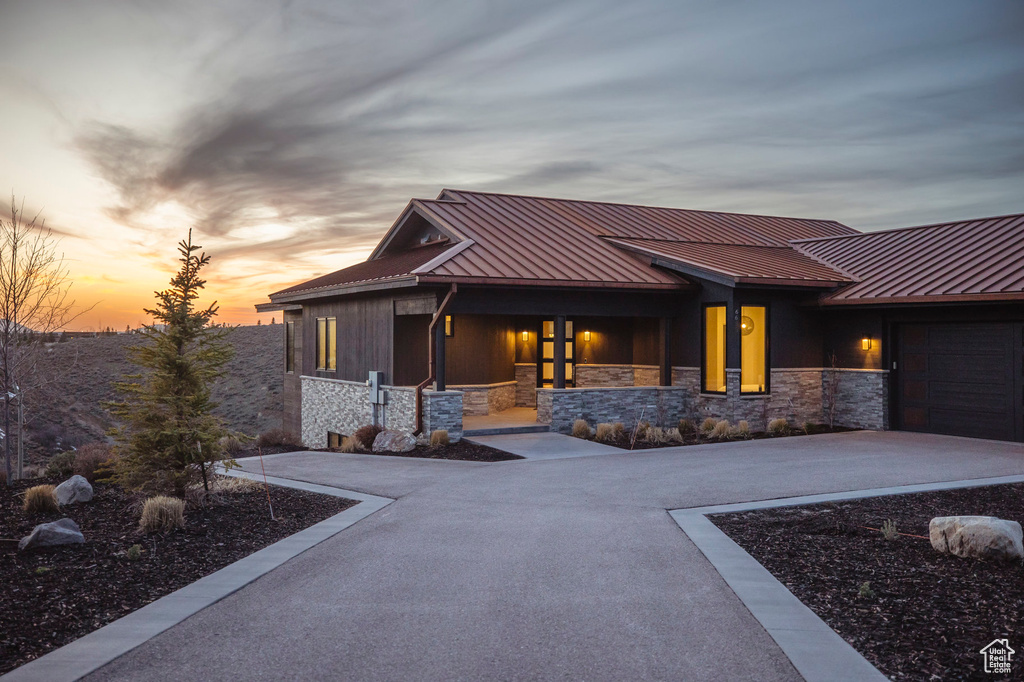 Back of house with concrete driveway, a standing seam roof, stone siding, and metal roof