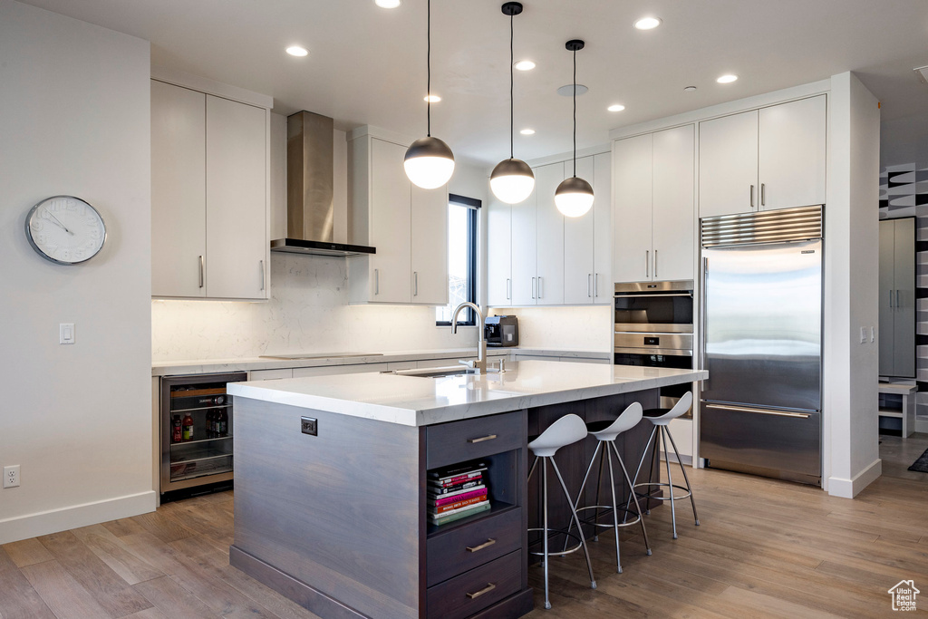 Kitchen with a kitchen bar, wall chimney range hood, a sink, beverage cooler, and stainless steel appliances