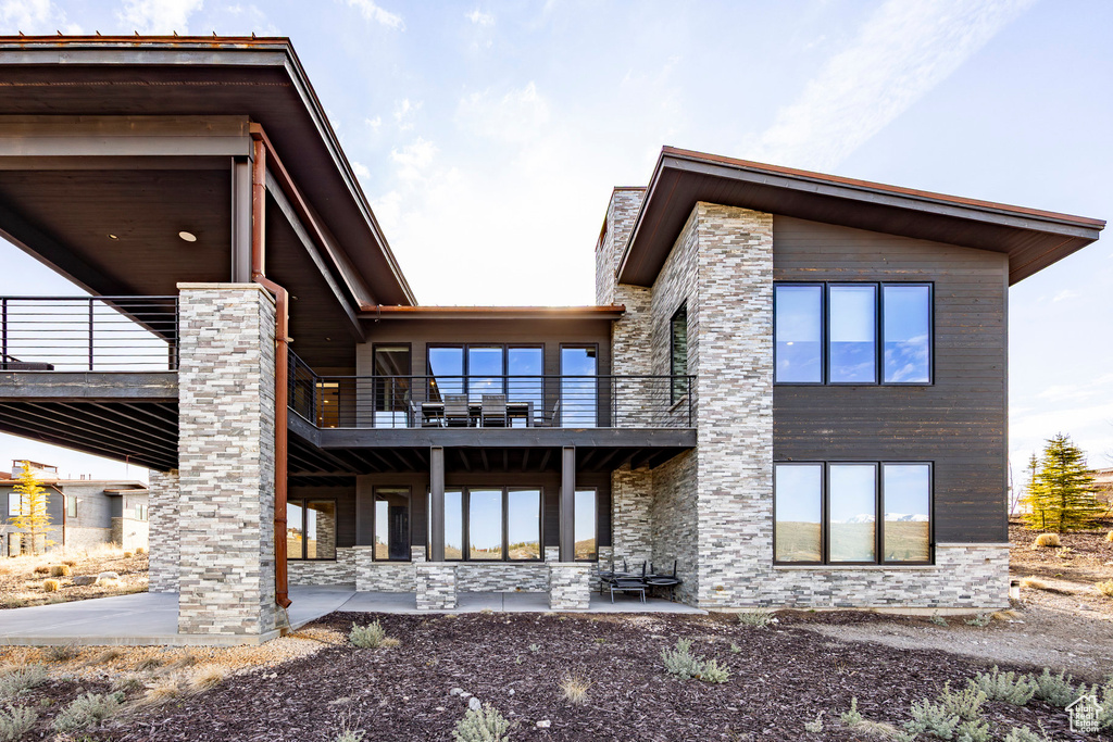 Rear view of house with a patio area, a balcony, and stone siding