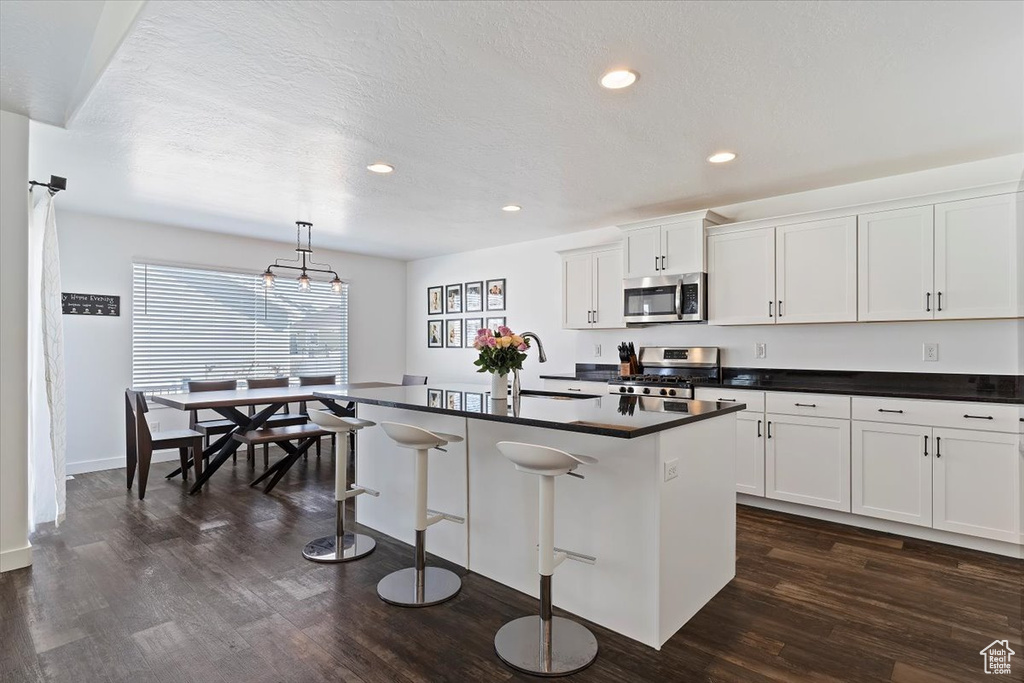 Kitchen featuring a kitchen breakfast bar, dark wood-style floors, dark countertops, stainless steel appliances, and a sink