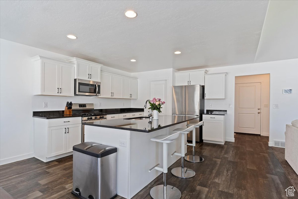 Kitchen with a sink, dark countertops, a kitchen bar, stainless steel appliances, and dark wood-type flooring
