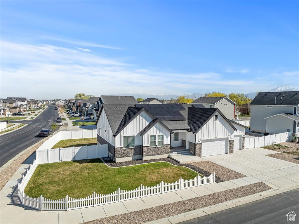 View of front of house featuring board and batten siding, roof mounted solar panels, a residential view, and a fenced front yard