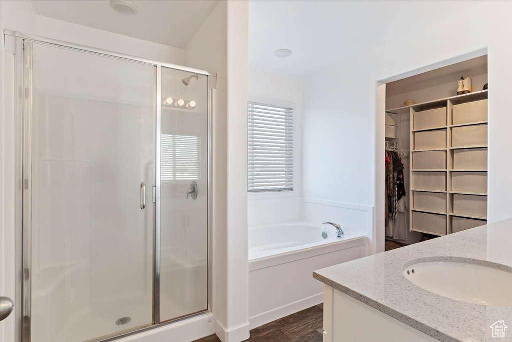 Bathroom with a bath, a spacious closet, a shower stall, vanity, and wood finished floors