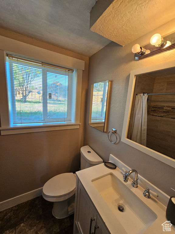 Bathroom with plenty of natural light, a textured ceiling, toilet, curtained shower, and vanity