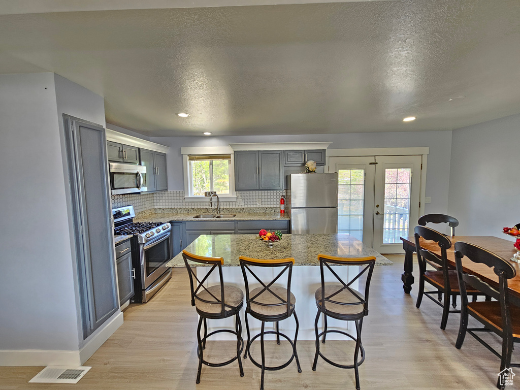 Kitchen with appliances with stainless steel finishes, a kitchen breakfast bar, backsplash, french doors, and a sink