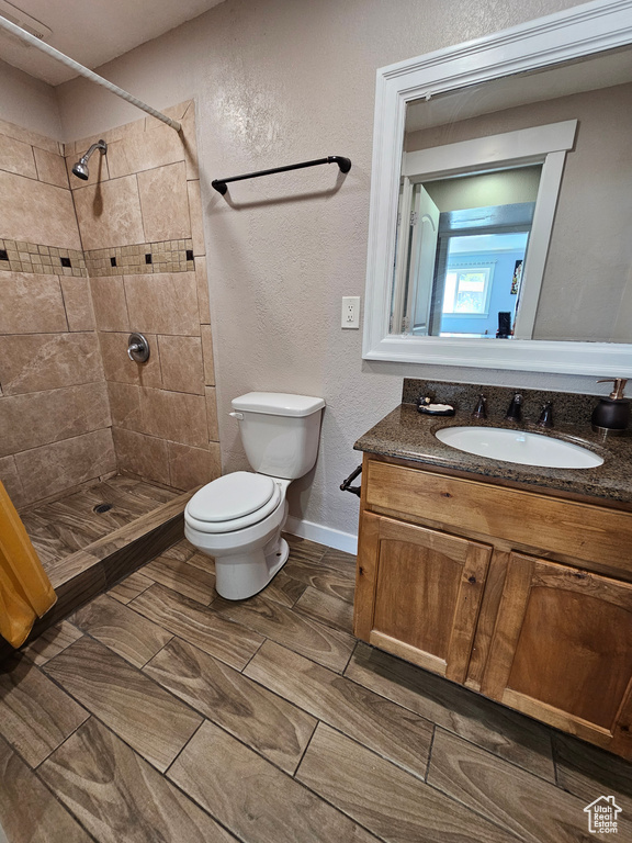 Full bath with toilet, a tile shower, vanity, a textured wall, and baseboards