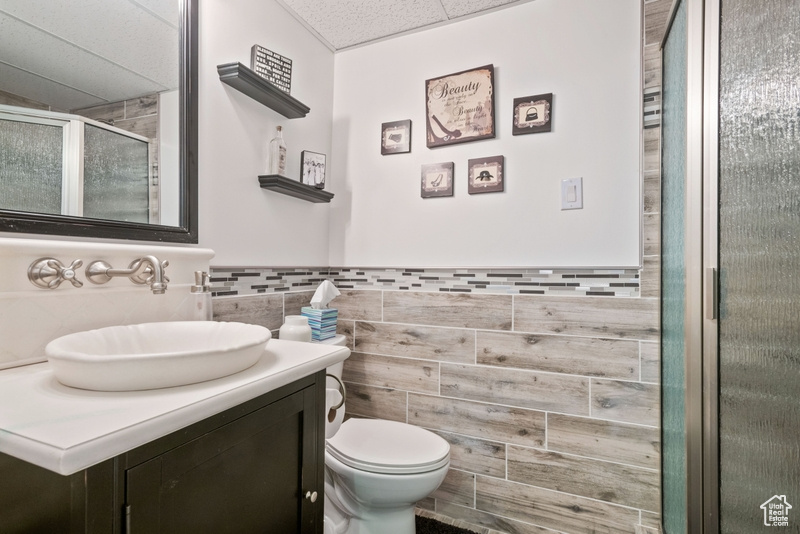 Full bath featuring a paneled ceiling, a shower stall, vanity, toilet, and tile walls