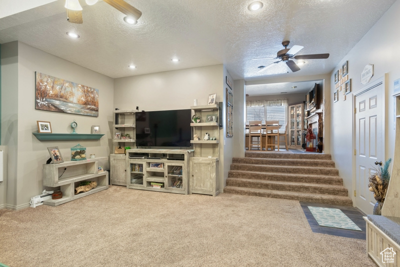 Living area featuring stairway, carpet floors, a textured ceiling, and ceiling fan