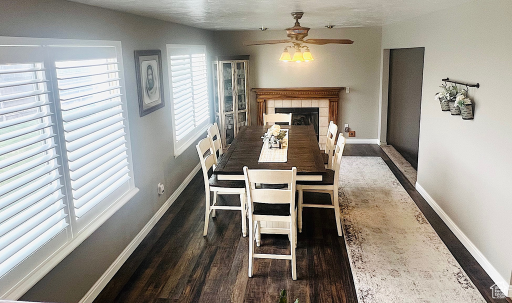 Dining area with wood finished floors, a tile fireplace, baseboards, and ceiling fan