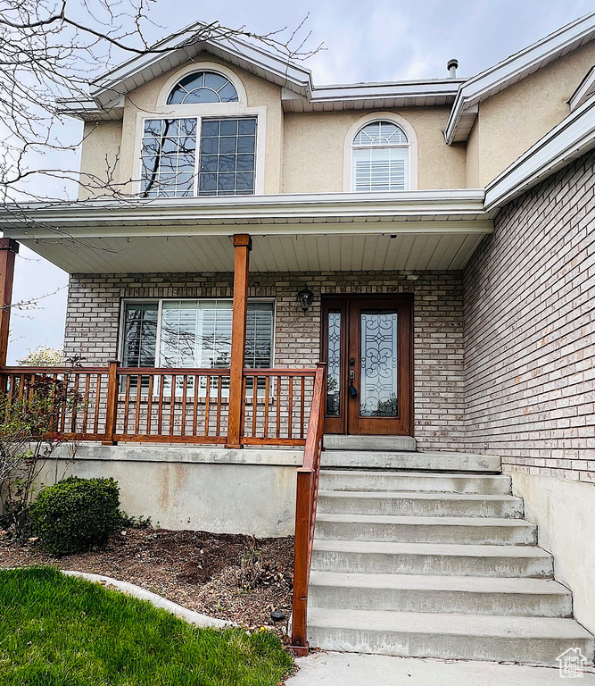 View of exterior entry featuring brick siding, a porch, and stucco siding