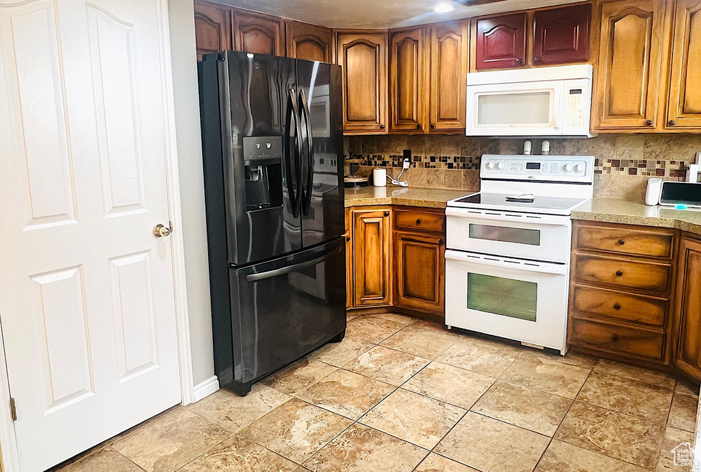 Kitchen featuring decorative backsplash, light countertops, white appliances, and brown cabinetry