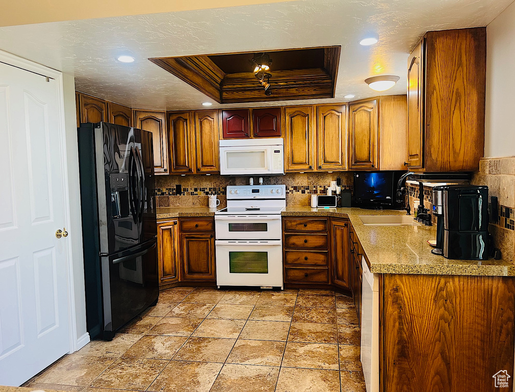 Kitchen featuring a tray ceiling, backsplash, a sink, and white appliances