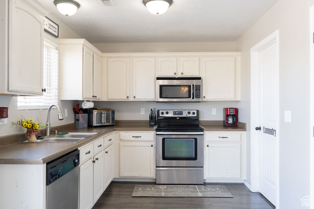 Kitchen featuring a sink, white cabinets, appliances with stainless steel finishes, and dark wood finished floors