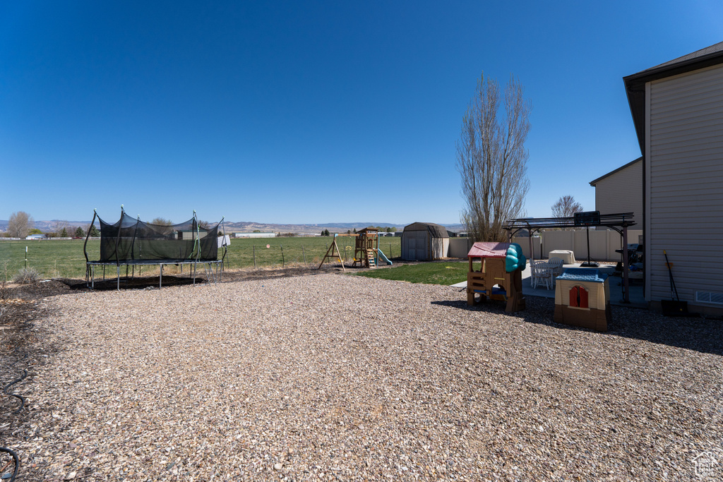 View of yard with a storage shed, a trampoline, fence, an outdoor structure, and a playground