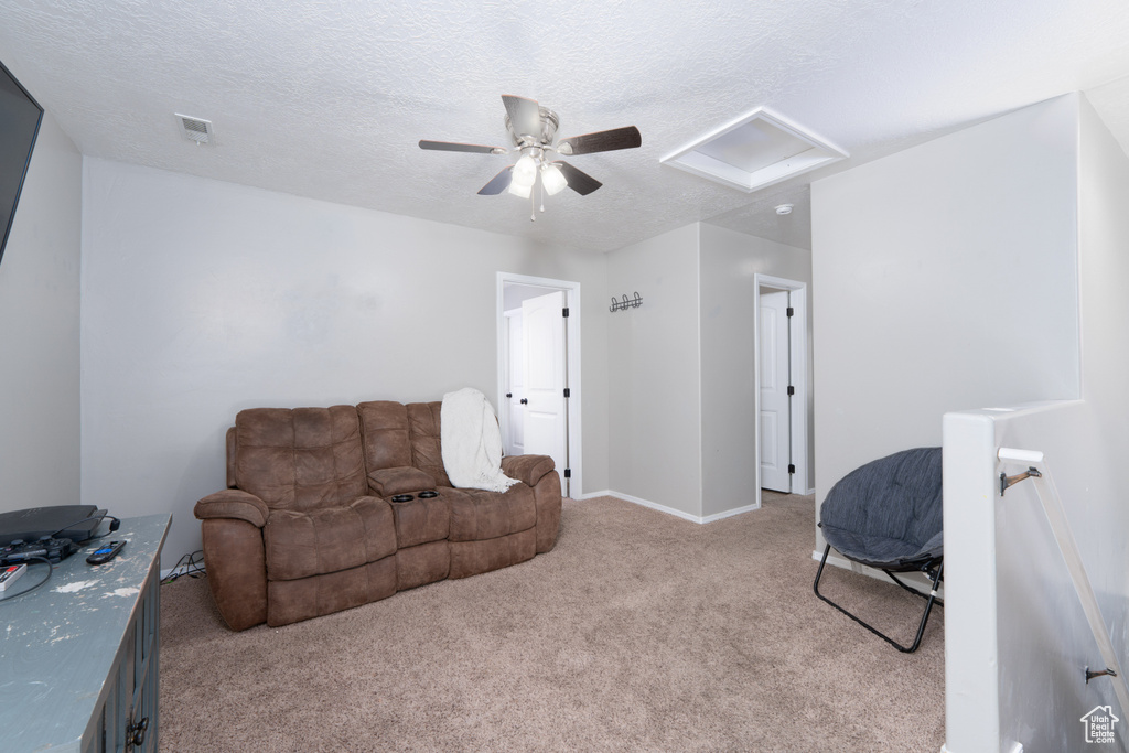 Living area with a textured ceiling, attic access, visible vents, ceiling fan, and light colored carpet