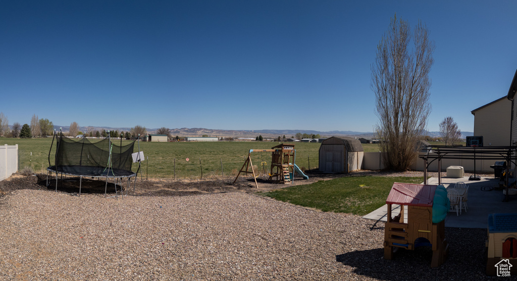 View of yard featuring a trampoline, fence, a playground, a storage unit, and an outbuilding