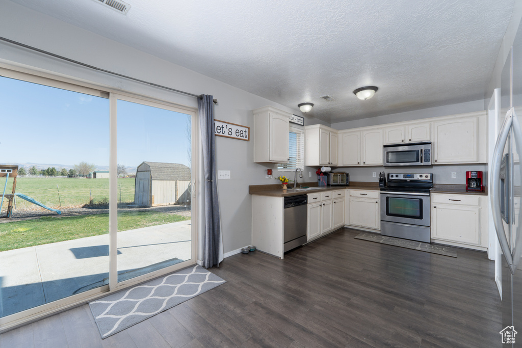 Kitchen with appliances with stainless steel finishes, a sink, dark countertops, and white cabinetry