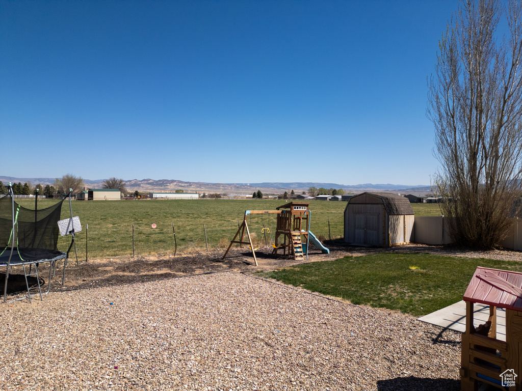 View of yard with an outbuilding, a shed, fence, a playground, and a trampoline