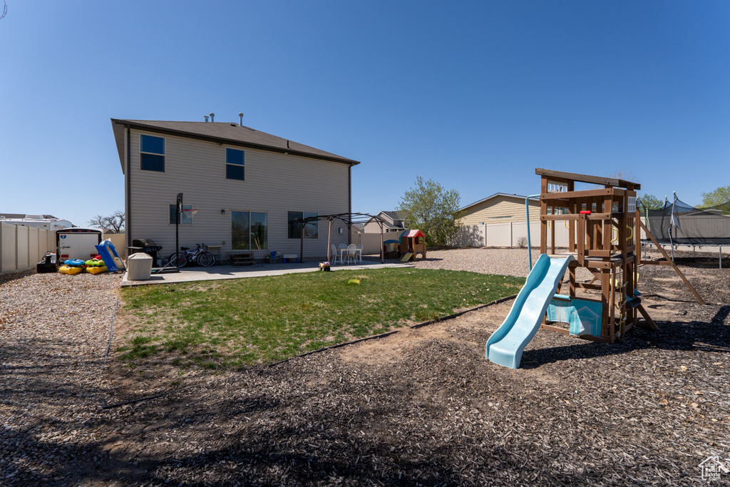 Rear view of property featuring a patio area, a trampoline, a lawn, a fenced backyard, and a playground