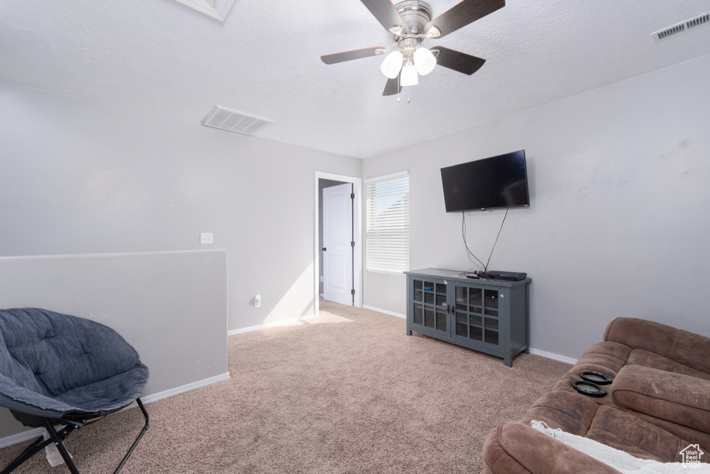 Carpeted living room with visible vents, baseboards, a ceiling fan, and a textured ceiling