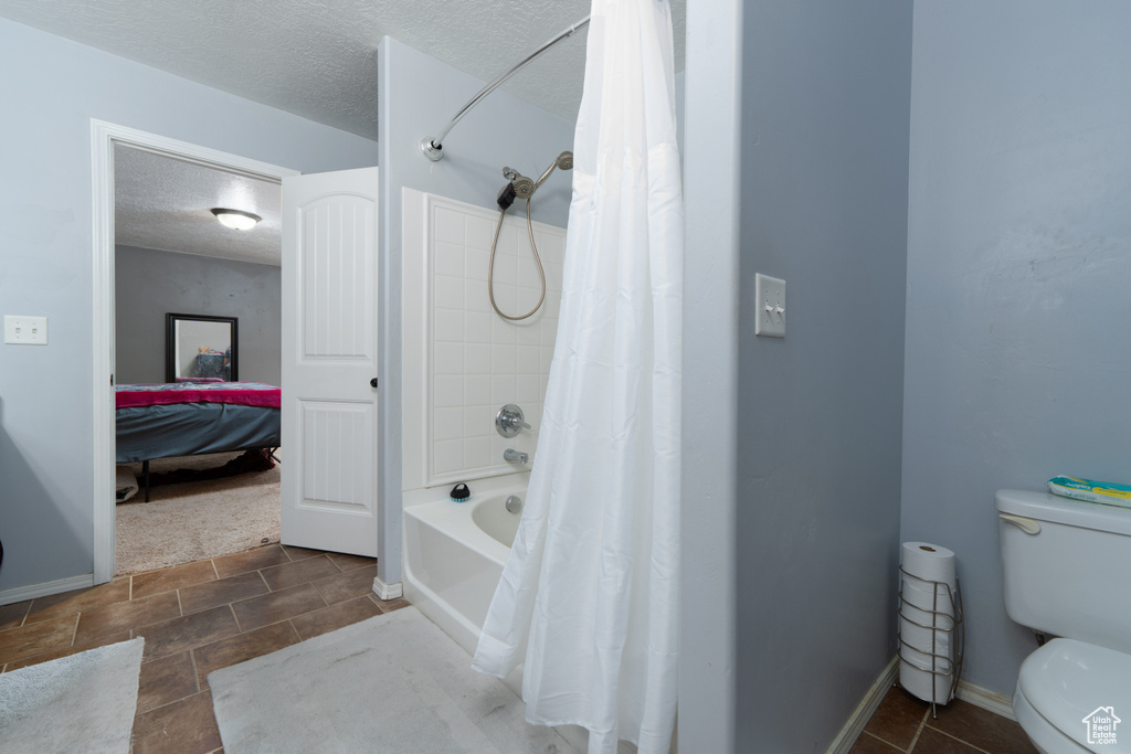 Full bathroom with toilet, a textured ceiling, shower / bathtub combination with curtain, and baseboards