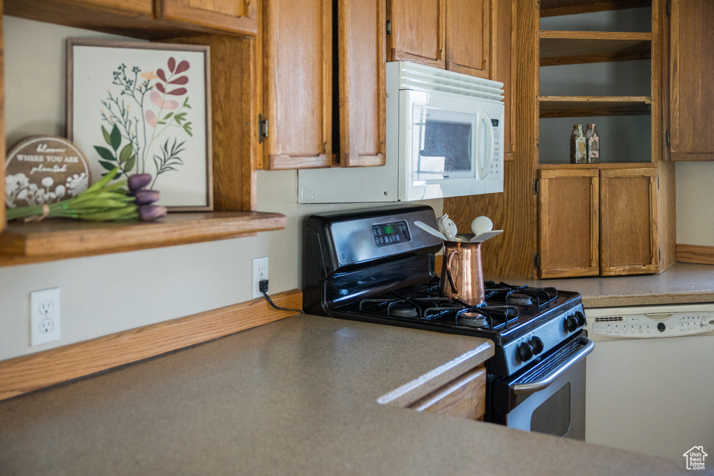 Kitchen with brown cabinetry, open shelves, light countertops, and white appliances