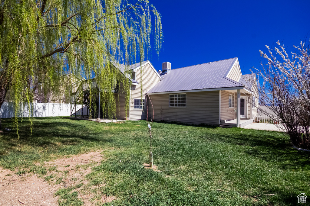 Back of house featuring fence, cooling unit, metal roof, and a lawn