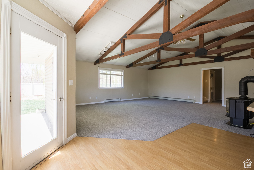 Unfurnished living room featuring lofted ceiling with beams, a wood stove, baseboards, and baseboard heating