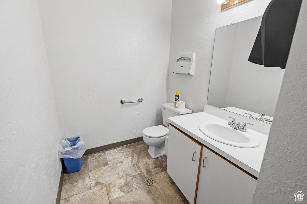 Half bathroom with toilet, stone finish floor, vanity, and baseboards