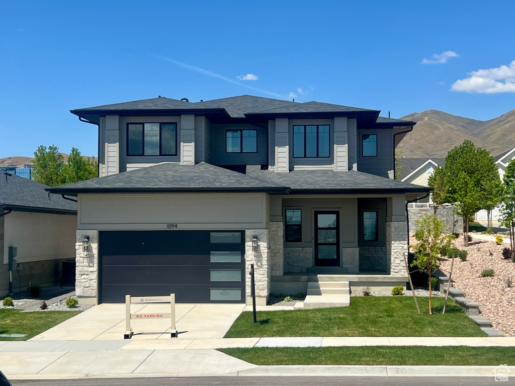 Prairie-style house featuring driveway, a garage, a mountain view, a front lawn, and stone siding