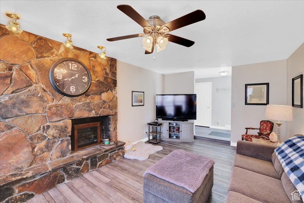 Living room featuring wood finished floors, baseboards, a ceiling fan, and a stone fireplace