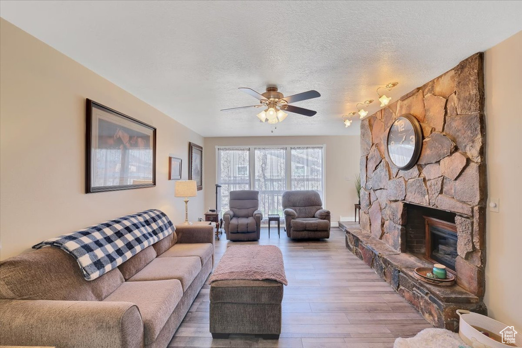 Living room featuring a textured ceiling, a ceiling fan, wood finished floors, and a fireplace