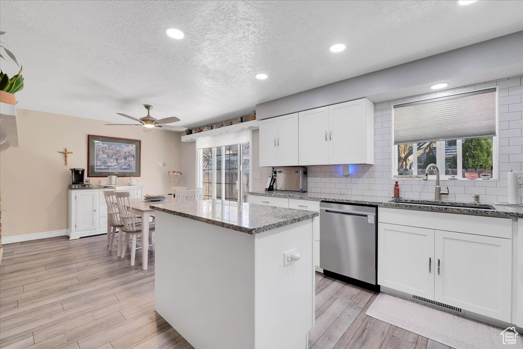 Kitchen with a textured ceiling, a ceiling fan, a kitchen island, stainless steel dishwasher, and a sink