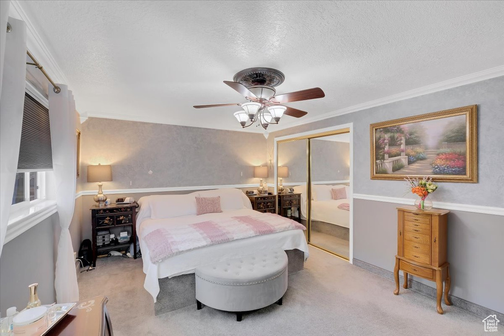 Bedroom with a closet, a textured ceiling, crown molding, ceiling fan, and light colored carpet