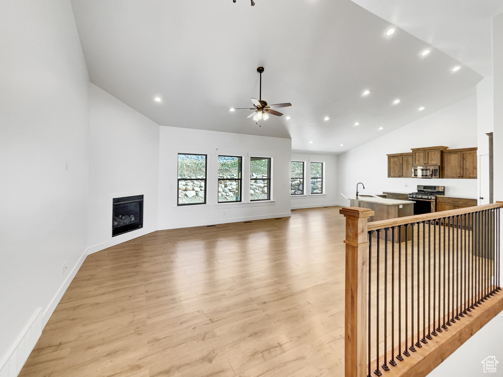 Unfurnished living room featuring ceiling fan, recessed lighting, vaulted ceiling, light wood-style flooring, and a glass covered fireplace